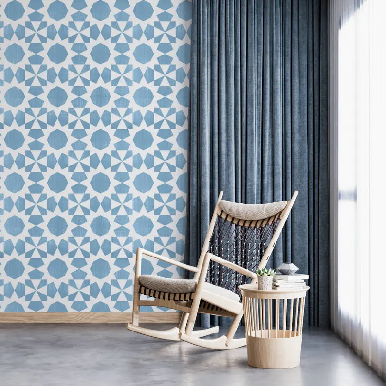Blue geometric patterned wallpaper with a cozy rocking chair and light blue curtains in a modern living space.