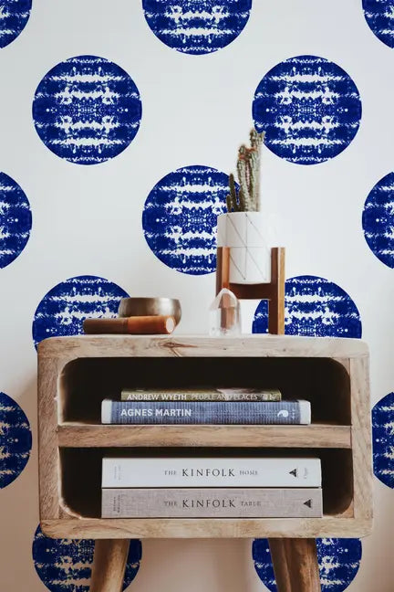 Blue and white circle-patterned wallpaper with a natural wood mid-century style side table, adorned with books and decor.
