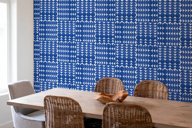 Navy blue geometric patterned wallpaper in a modern dining room, paired with a rustic wooden table and wicker chairs.