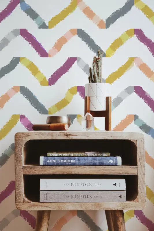Wooden side table with open shelves, styled with books, a crystal, and a potted cactus against colorful zigzag wallpaper.