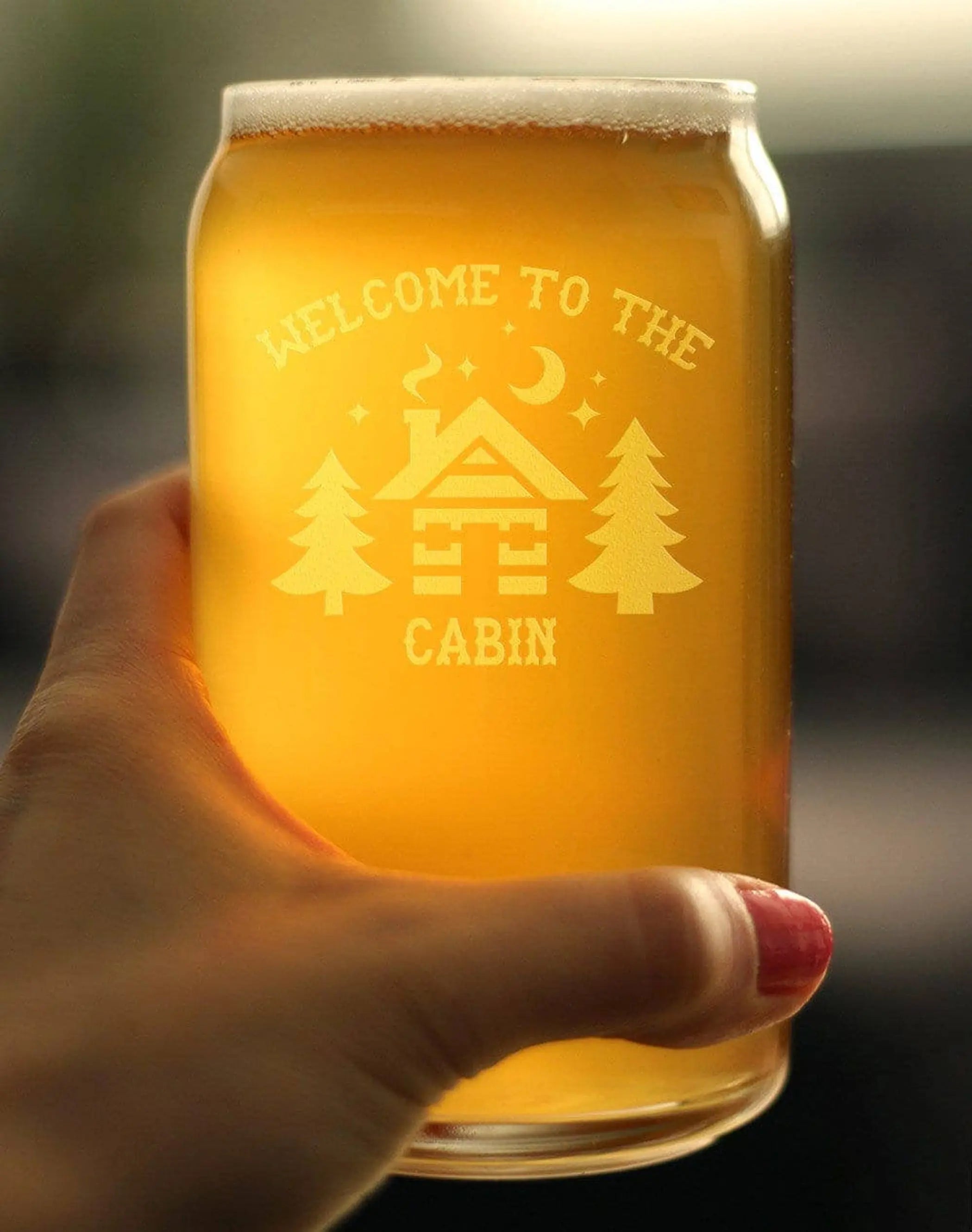 Engraved glass beer mug with amber beverage, featuring a cabin design and pine trees, perfect for cabin-themed gatherings.