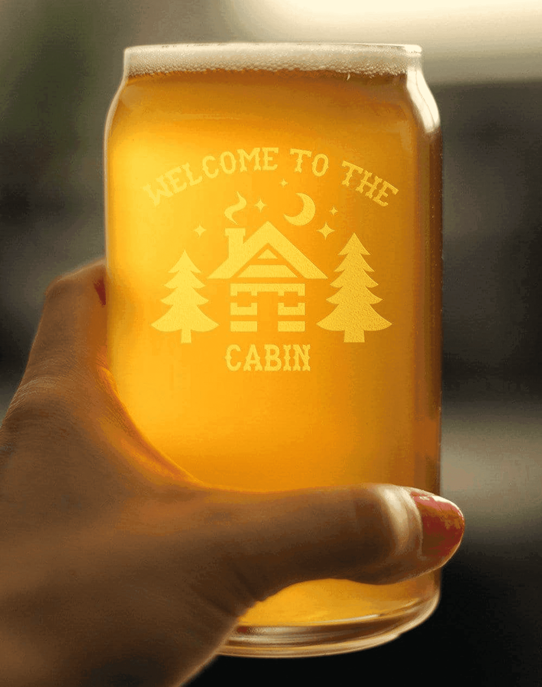 Engraved glass beer mug with amber beverage, featuring a cabin design and pine trees, perfect for cabin-themed gatherings.