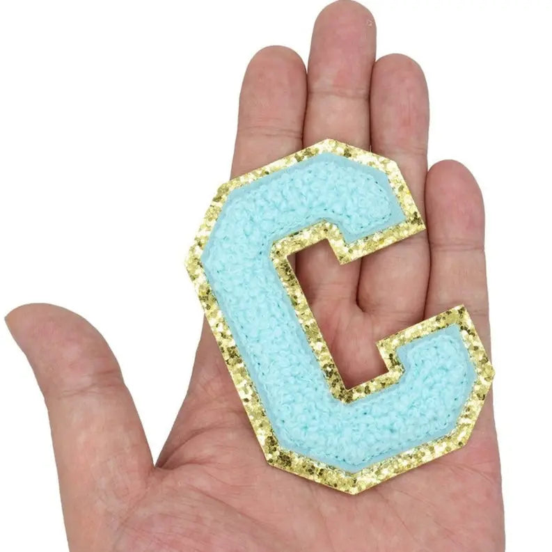 Aqua blue glitter letter "C" patch with gold trim, perfect for DIY projects or personalizing accessories.