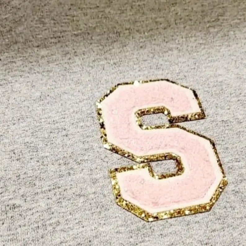 Grey sweatshirt featuring a pink and gold glitter varsity letter "S" applique. Perfect for casual, stylish wear.
