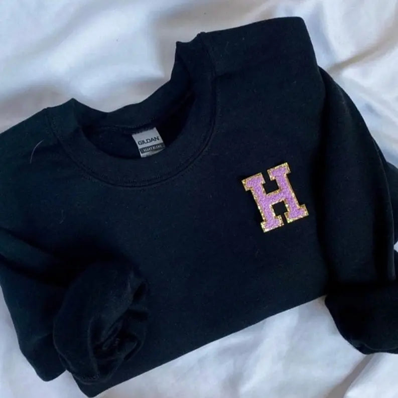 Black sweatshirt featuring a glittery purple "H" logo, stylish and cozy for casual wear.