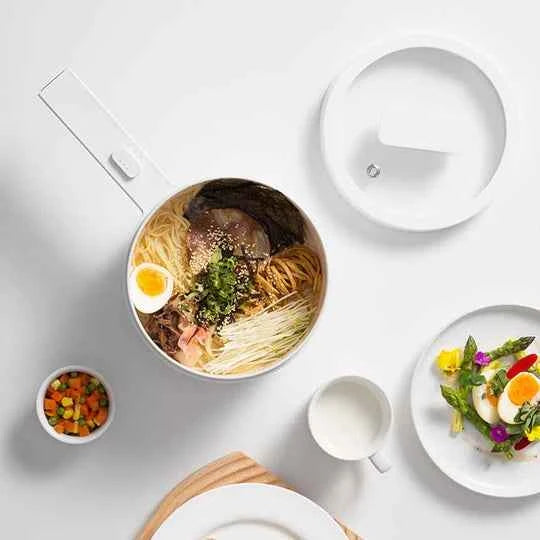 White bowl with ramen noodles, beef, soft-boiled egg, and vegetables, served with colorful side dish and cream.